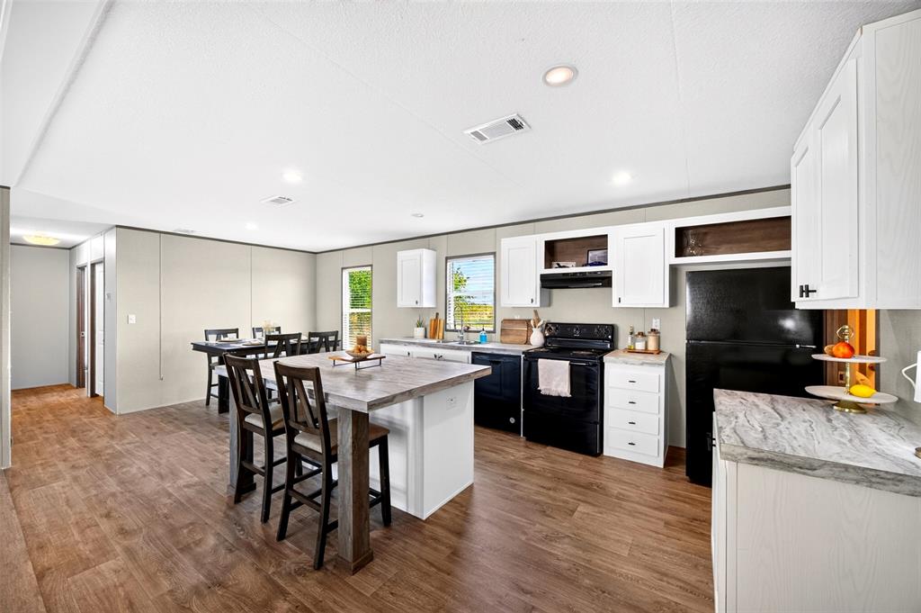 3208 Northeast County Road Powell, TX 75153 - Photo 7 of 29 Open-concept living space with wood-finish flooring, recessed lighting, a kitchen island with seating, white cabinetry, and black appliances