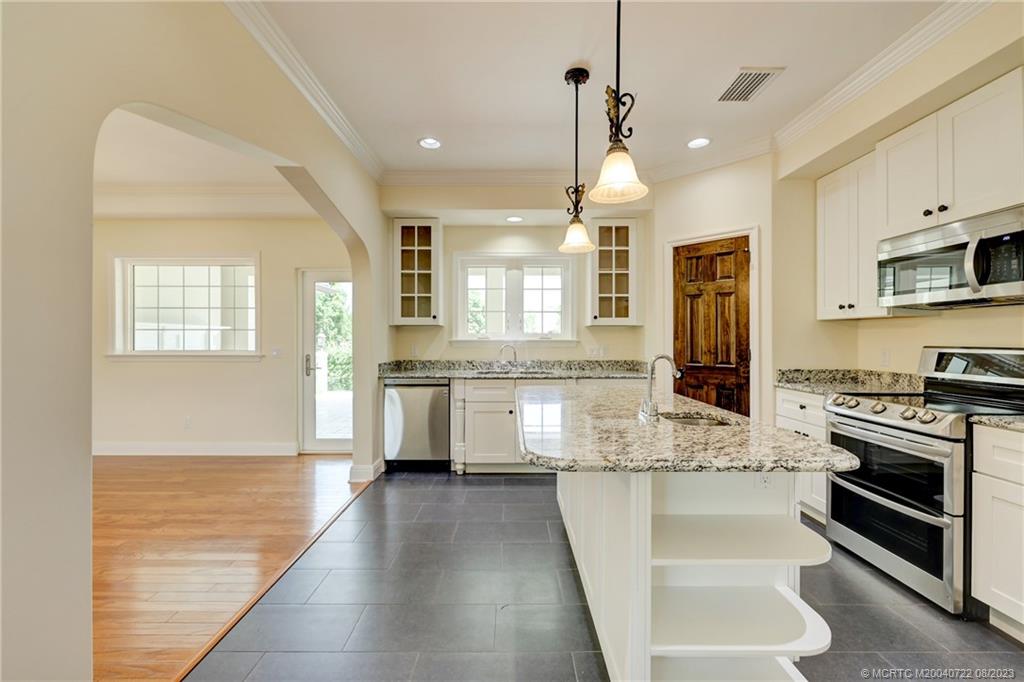 4865 Southeast Manatee Cove Road Stuart, FL 34997 - Photo 24 of 53 a large kitchen with kitchen island a stove a sink a refrigerator and white cabinets with wooden floor