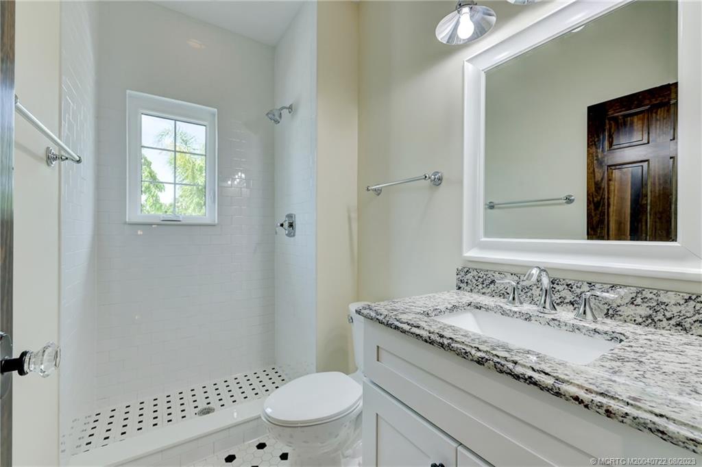 4865 Southeast Manatee Cove Road Stuart, FL 34997 - Photo 39 of 53 a bathroom with a granite countertop sink a toilet a mirror and shower