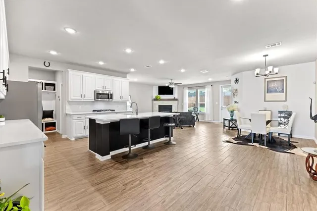a living room with stainless steel appliances kitchen island granite countertop a table chairs and a refrigerator