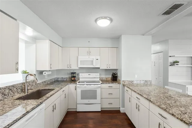 a kitchen with granite countertop white cabinets sink and white appliances