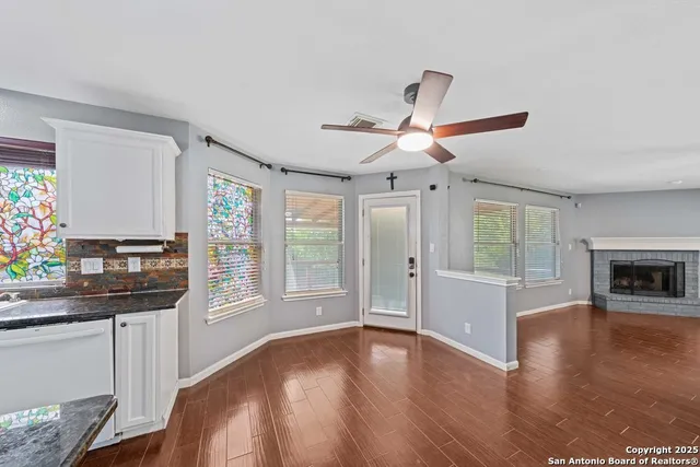 a view of a livingroom with a fireplace a ceiling fan and wooden floor