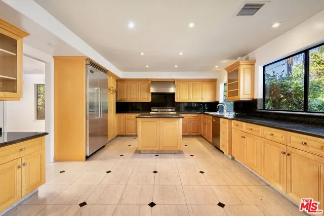 a large kitchen with stainless steel appliances kitchen island granite countertop a refrigerator a sink dishwasher and white cabinets with wooden floor