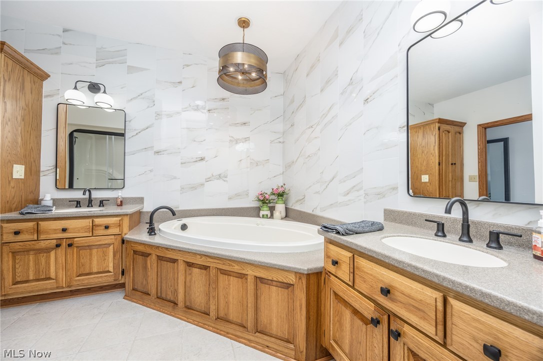 1602 Glendale Road, Unit 3 Marietta, OH 45750 - Photo 21 of 49 Soaking tub with surrounding wood-finish cabinetry, dual vanities with integrated sinks, matte black fixtures, and white marble-look wall tiling