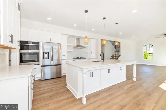 a kitchen with stainless steel appliances kitchen island granite countertop a refrigerator a stove a sink and white cabinets