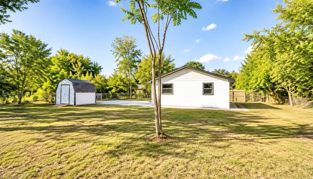 7061 Base Street Azle, TX 76020 - Photo 13 of 13 Expansive grassy yard featuring a gabled storage shed, concrete patio, and a chain-link fence