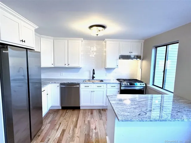 a kitchen with stainless steel appliances granite countertop a stove a sink dishwasher a refrigerator and white cabinets with wooden floor