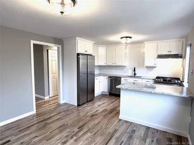 a kitchen with stainless steel appliances granite countertop a refrigerator a sink dishwasher a stove and white countertops with wooden floor