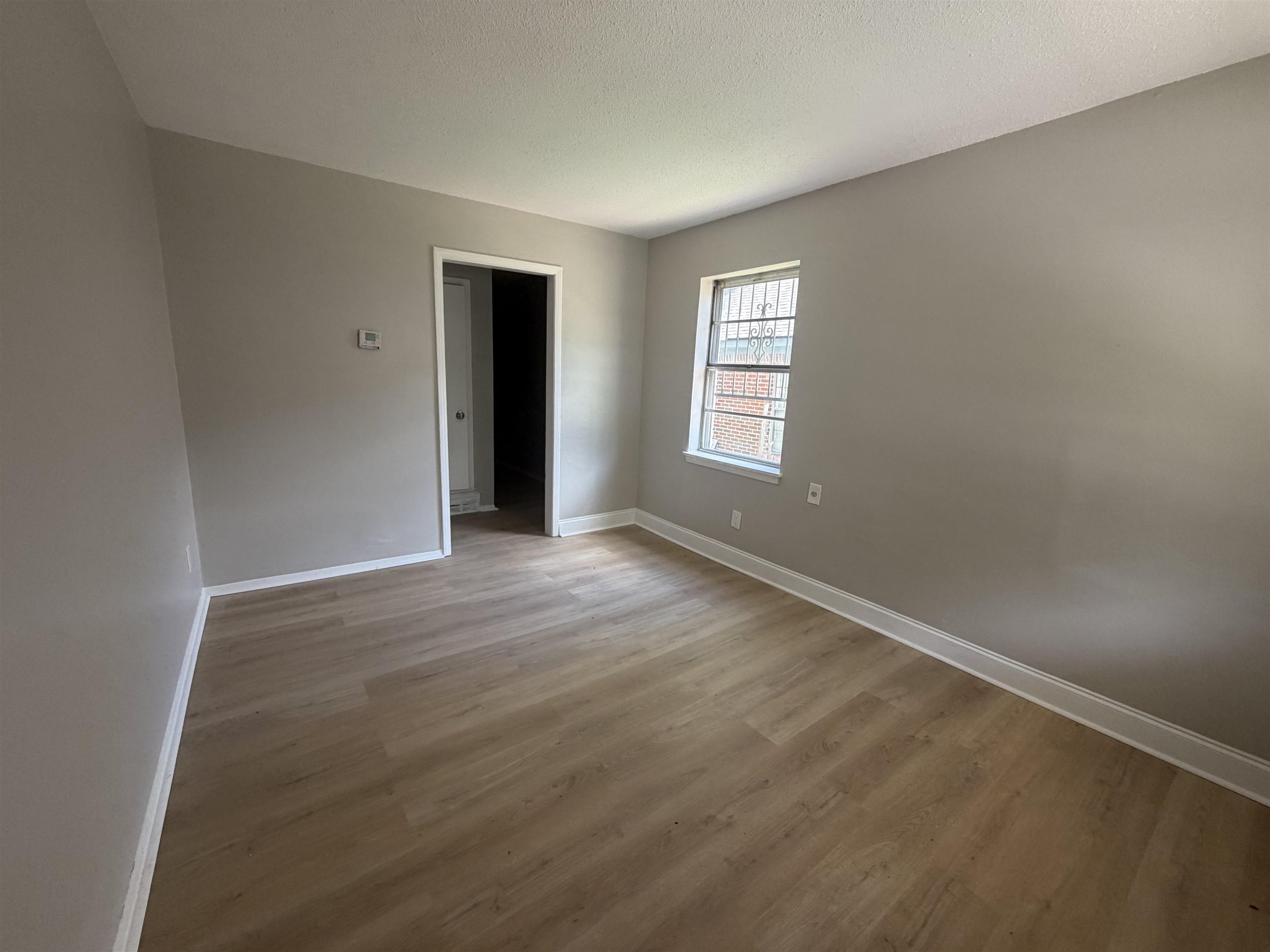 2402 Shasta Avenue Memphis, TN 38108 - Photo 7 of 7 Spacious room featuring wood-finish flooring, light gray walls, white trim, and a window with security bars