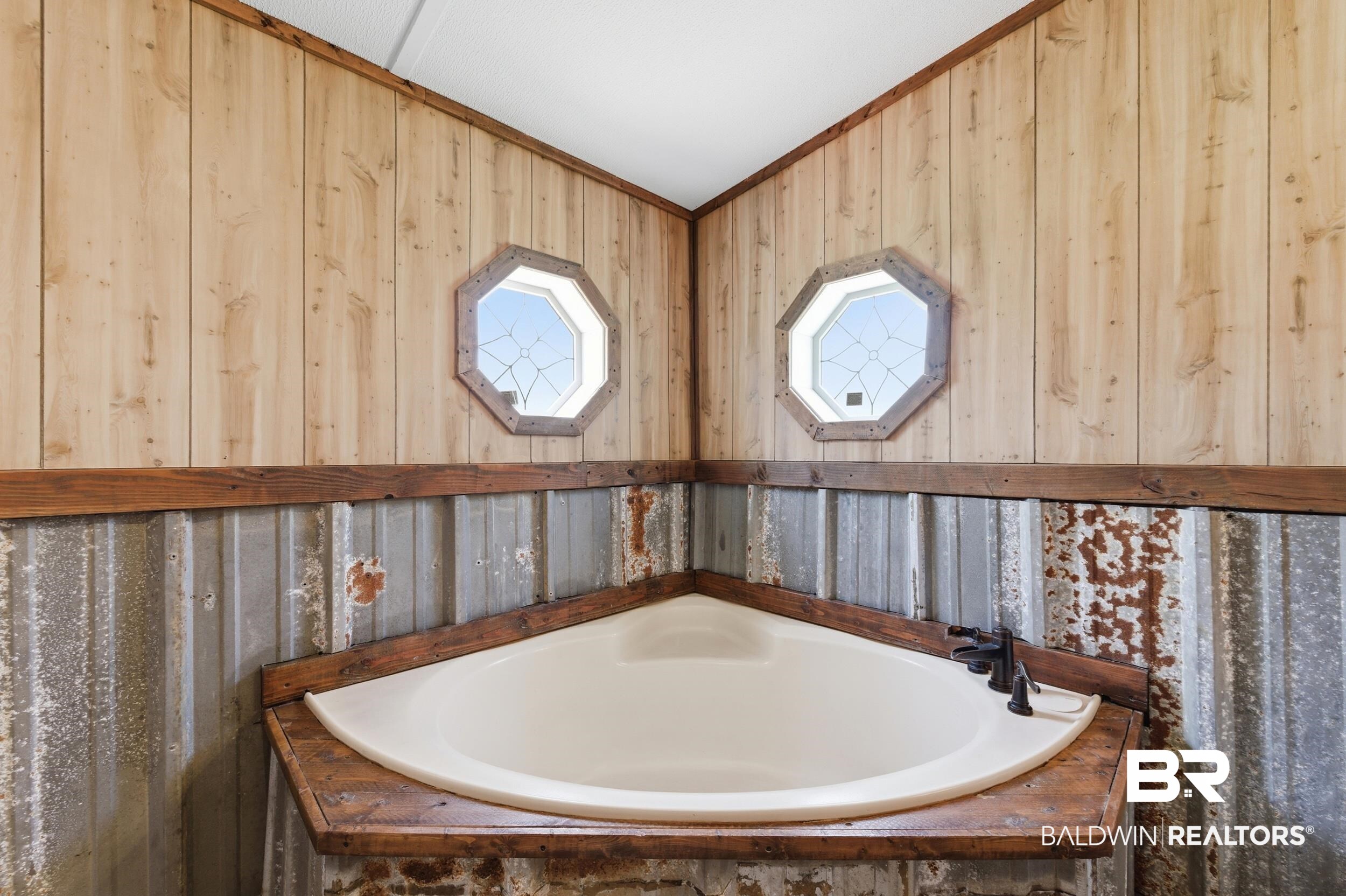 926 Tumbling Lane Atmore, AL 36502 - Photo 31 of 56 Corner soaking tub with a dark bronze faucet, surrounded by wood paneling, corrugated metal accents, and two octagon-shaped windows