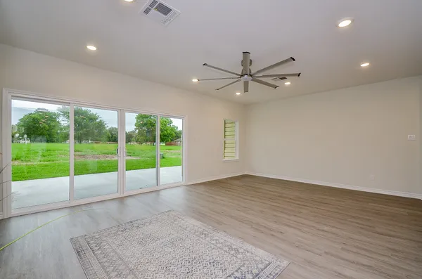 a view of an empty room with window a ceiling fan and wooden floor