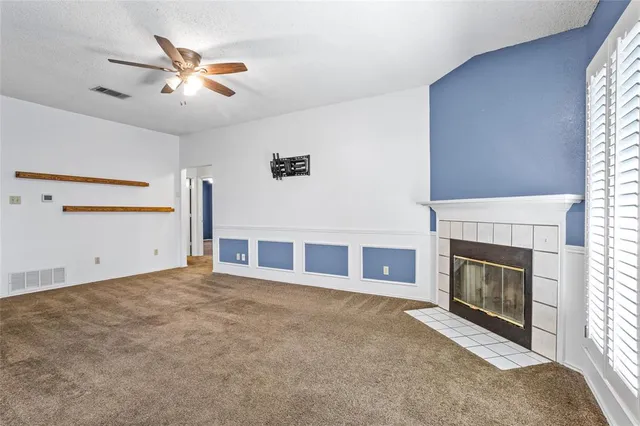 a view of a livingroom with a fireplace a ceiling fan and windows