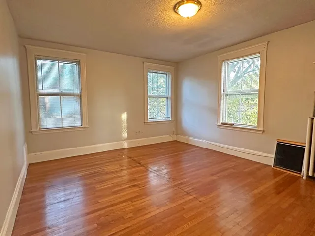 a view of an empty room with wooden floor and windows