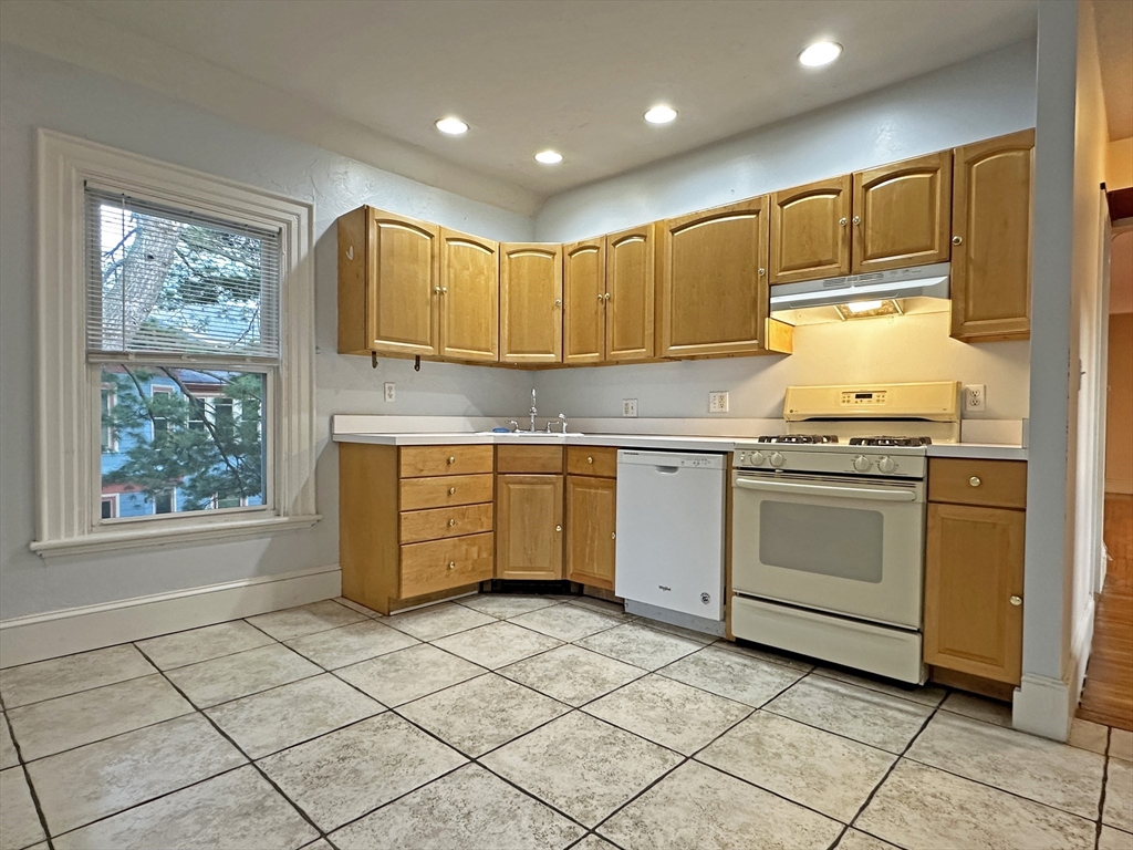 399 Newtonville Avenue, Unit 2 Newton, MA 02460 - Photo 7 of 24 a kitchen with a stove a sink dishwasher and white cabinets with wooden floor