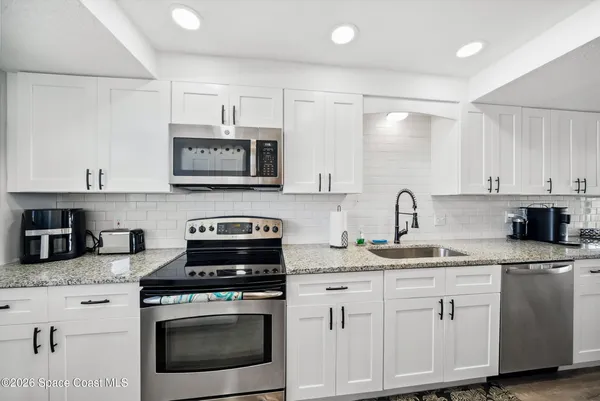a kitchen with granite countertop white cabinets white stainless steel appliances and a sink