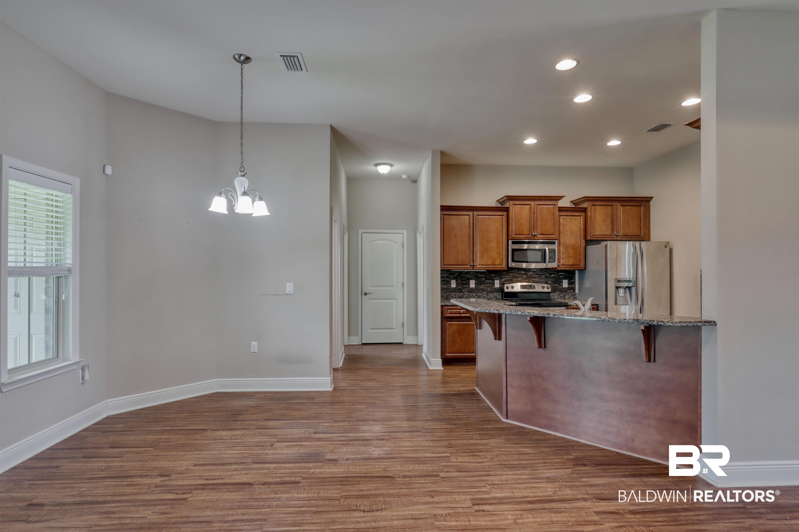 14794 Troon Drive Foley, AL 36535 - Photo 9 of 33 Kitchen with a breakfast bar, baseboards, dark wood-style floors, brown cabinets, and stainless steel appliances