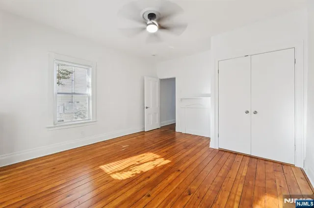 a view of an empty room with wooden floor and a ceiling fan