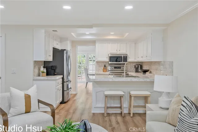 a living room with stainless steel appliances furniture a fireplace a flat screen tv and a kitchen view