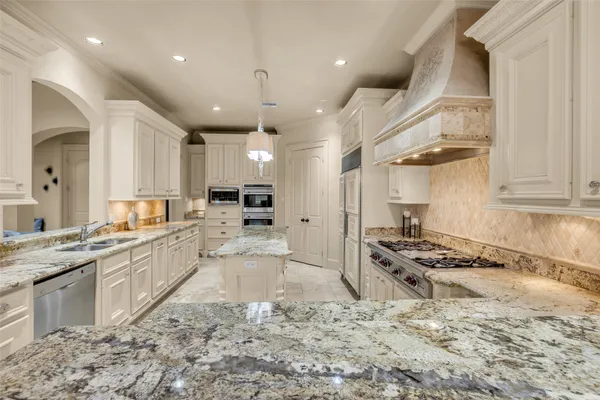 a large kitchen with stainless steel appliances kitchen island granite countertop a large stove a sink dishwasher and white cabinets with wooden floor