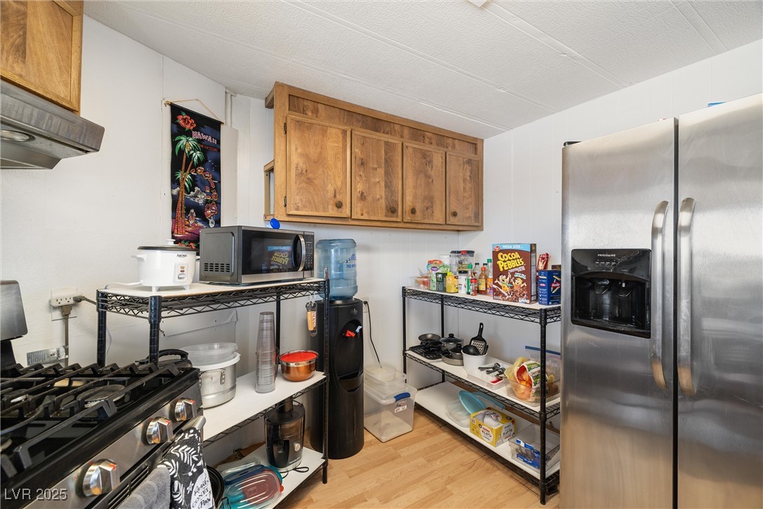 3581 West Dyer Road Pahrump, NV 89048 - Photo 12 of 31 Kitchen with appliances with stainless steel finishes, brown cabinetry, light wood-style floors, and extractor fan