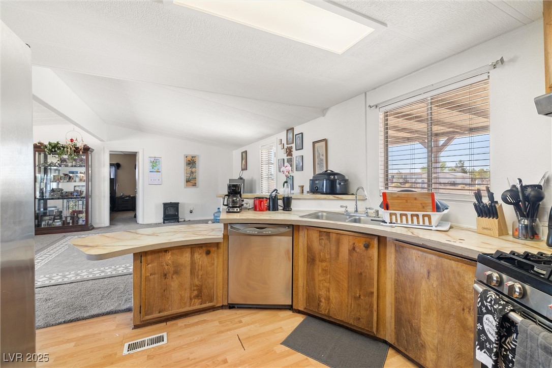 3581 West Dyer Road Pahrump, NV 89048 - Photo 13 of 31 Kitchen featuring stainless steel appliances, light countertops, light wood finished floors, lofted ceiling, and brown cabinets