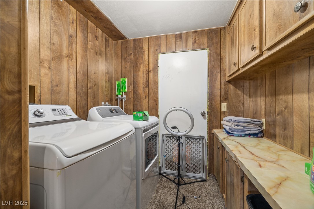 3581 West Dyer Road Pahrump, NV 89048 - Photo 22 of 31 Laundry room featuring wooden walls, washing machine and dryer, and cabinet space