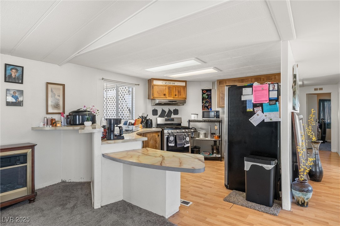 3581 West Dyer Road Pahrump, NV 89048 - Photo 9 of 31 Kitchen with a peninsula, appliances with stainless steel finishes, light countertops, brown cabinetry, and light wood finished floors