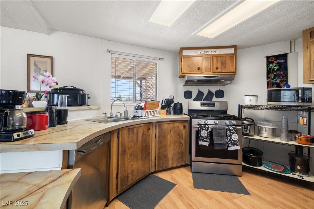 3581 West Dyer Road Pahrump, NV 89048 - Photo 10 of 31 Kitchen with stainless steel appliances, light wood-style floors, brown cabinetry, light countertops, and under cabinet range hood