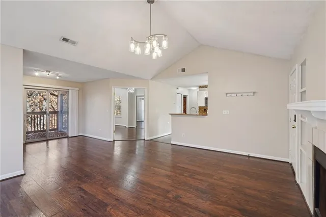 a view of an empty room with wooden floor and a kitchen