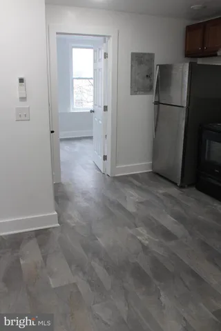 a view of a refrigerator in kitchen and an empty room with wooden floor windows