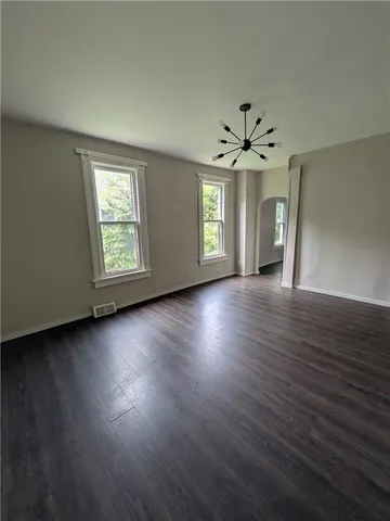 an empty room with wooden floor chandelier fan and windows
