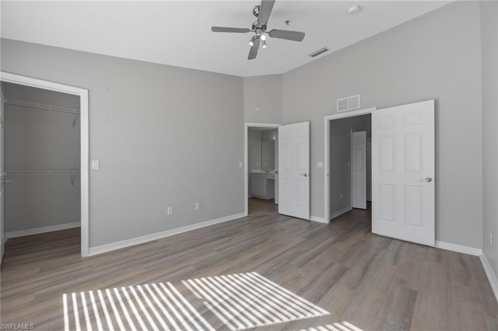 15930 Marcello Circle, Unit 242 Naples, FL 34110 - Photo 15 of 32 an empty room with wooden floor chandelier fan and windows