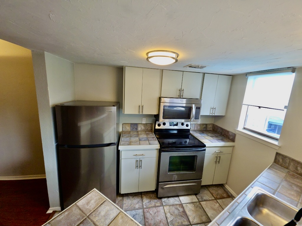 2500 Burleson Road, Unit 521 Austin, TX 78741 - Photo 8 of 20 Kitchen featuring stainless steel appliances, light-toned cabinetry, tile flooring, tile countertops, and a double basin sink