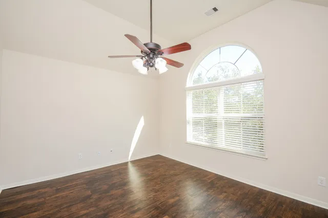 an empty room with wooden floor fan and windows