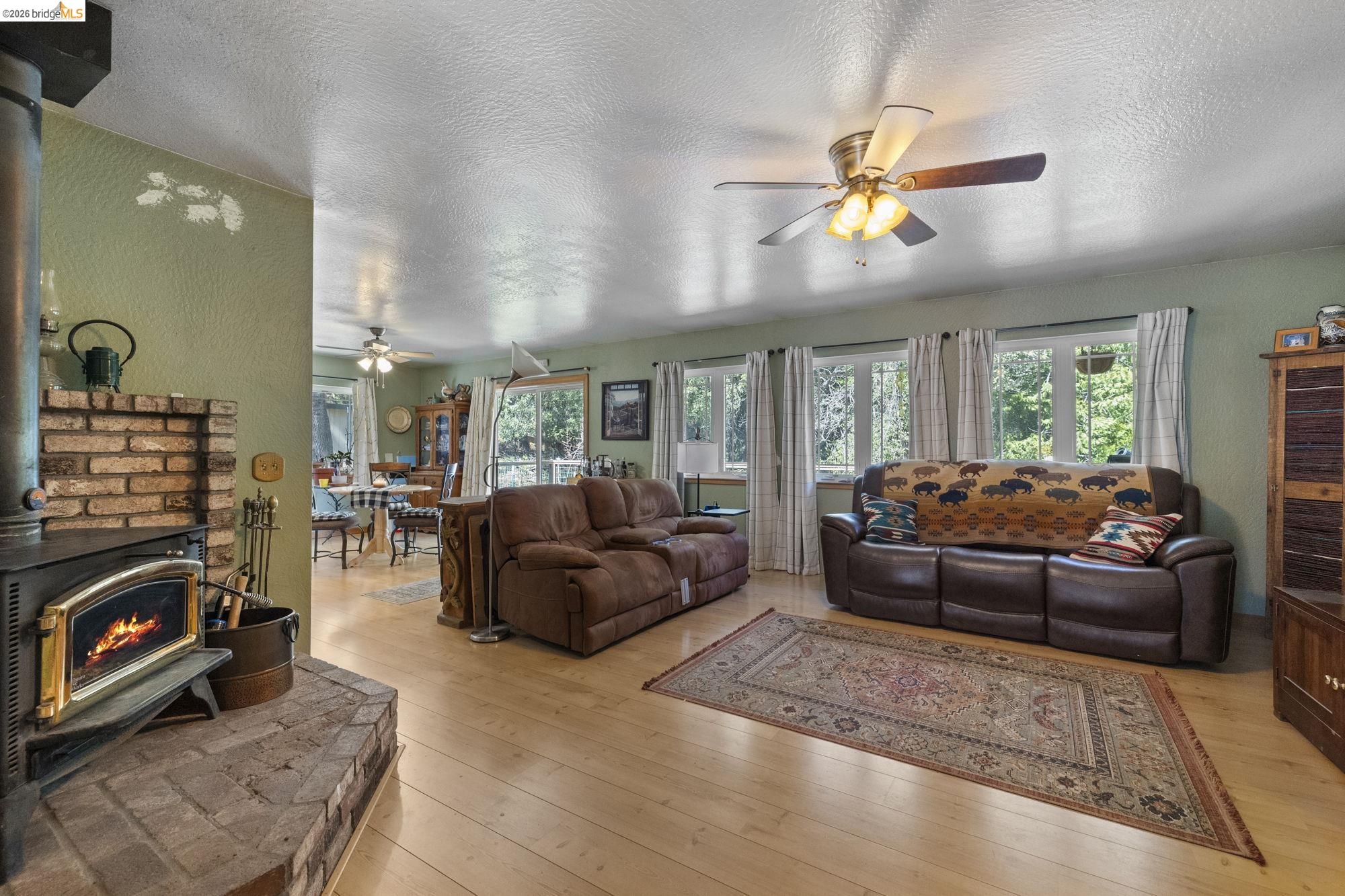 23615 Elizabeth Peak Road Twain Harte, CA 95383 - Photo 6 of 38 Living room with a wood stove, a textured ceiling, a ceiling fan, light wood-style flooring, and plenty of natural light