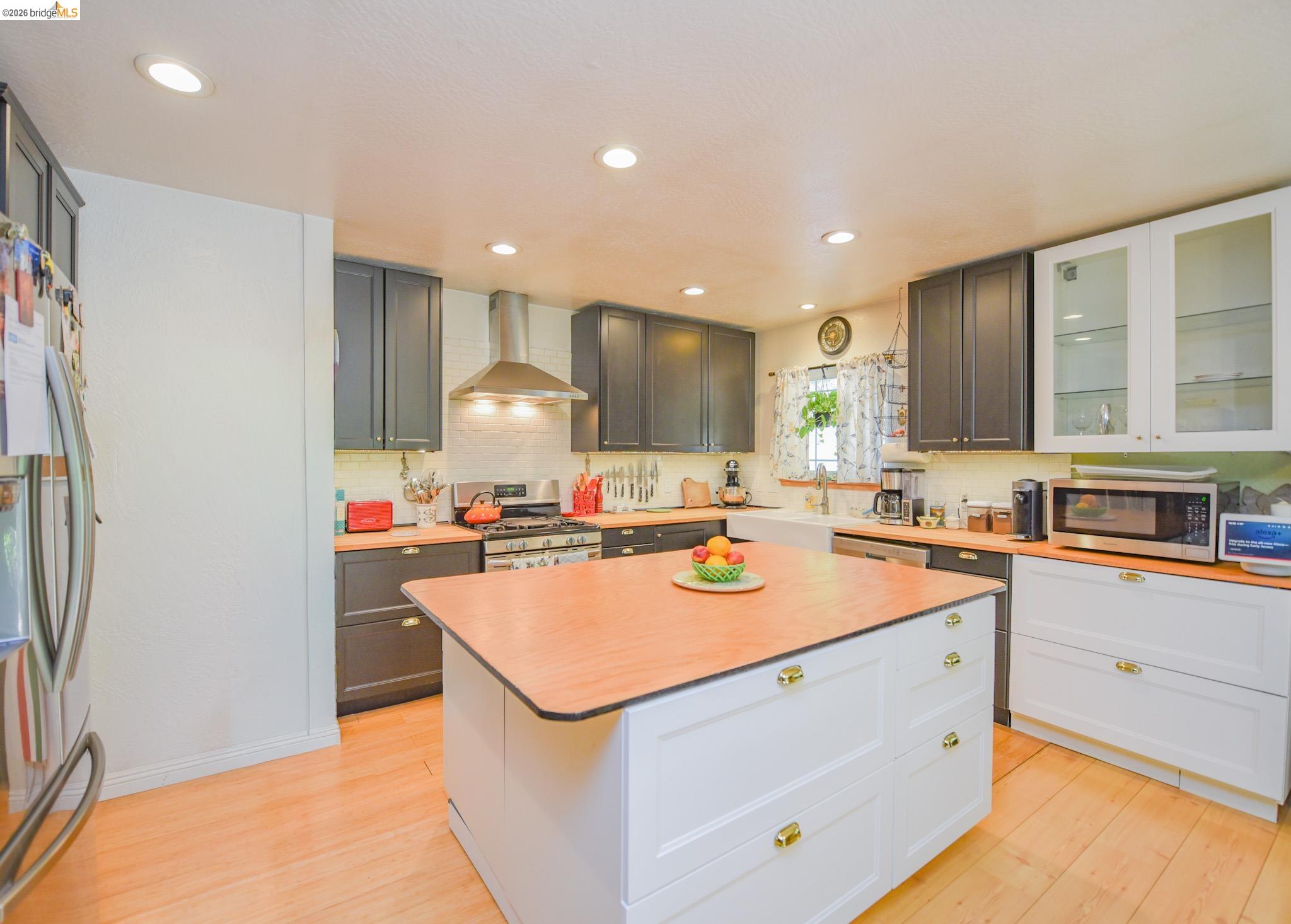 23615 Elizabeth Peak Road Twain Harte, CA 95383 - Photo 9 of 38 Kitchen with appliances with stainless steel finishes, wall chimney exhaust hood, glass insert cabinets, light wood-style flooring, and a center island
