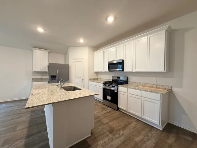 a kitchen with stainless steel appliances granite countertop a sink dishwasher stove top oven and refrigerator with wooden floor