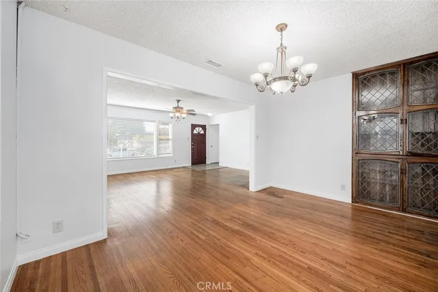 an empty room with wooden floor chandelier and windows