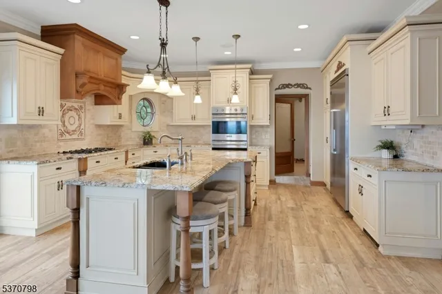 a kitchen with stainless steel appliances kitchen island granite countertop a stove a sink a refrigerator and white cabinets with wooden floor