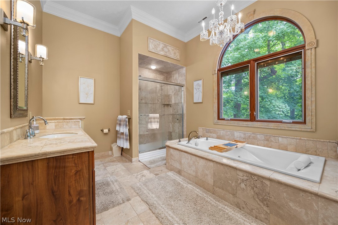 7587 Lewis Road Olmsted Falls, OH 44138 - Photo 38 of 50 Arched window with decorative surround, built-in soaking tub, tiled walk-in shower with glass enclosure, wood-finish vanity with stone countertop, and crystal chandelier
