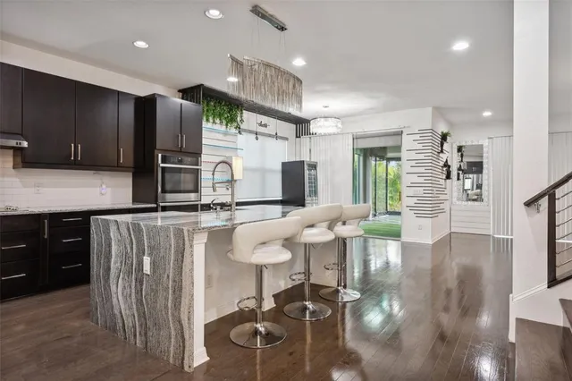 a kitchen with stainless steel appliances kitchen island granite countertop a refrigerator a stove a sink and a dining table with wooden floor