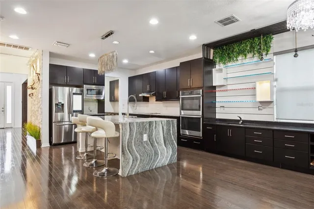 a kitchen with stainless steel appliances kitchen island granite countertop a refrigerator a stove a sink dishwasher and a dining table with wooden floor
