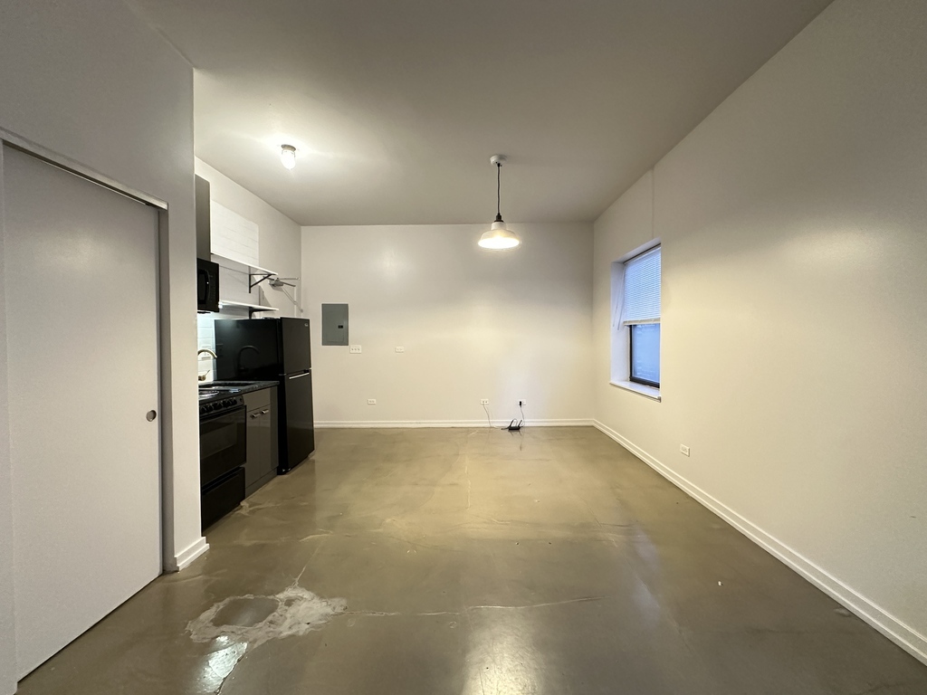 1136 West Wilson Avenue, Unit 217 Chicago, IL 60640 - Photo 12 of 19 an empty room with kitchen view and a refrigerator