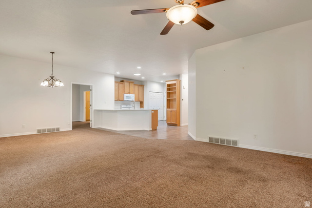 1092 Tithing Ridge Drive Riverton, UT 84065 - Photo 6 of 25 Open-concept living space featuring carpeted flooring, a ceiling fan with integrated lighting, a chandelier, a kitchen with light wood cabinetry, and a peninsula counter