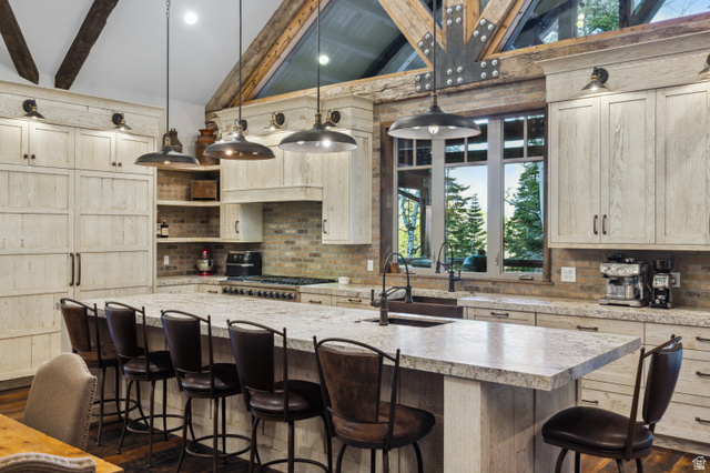1667 West Tollgate Cyn Road Coalville, UT 84017 - Photo 23 of 61 Expansive kitchen featuring a large island with countertop seating, stone countertops, a full-height brick backsplash, exposed wood beam ceiling, and multiple pendant light fixtures