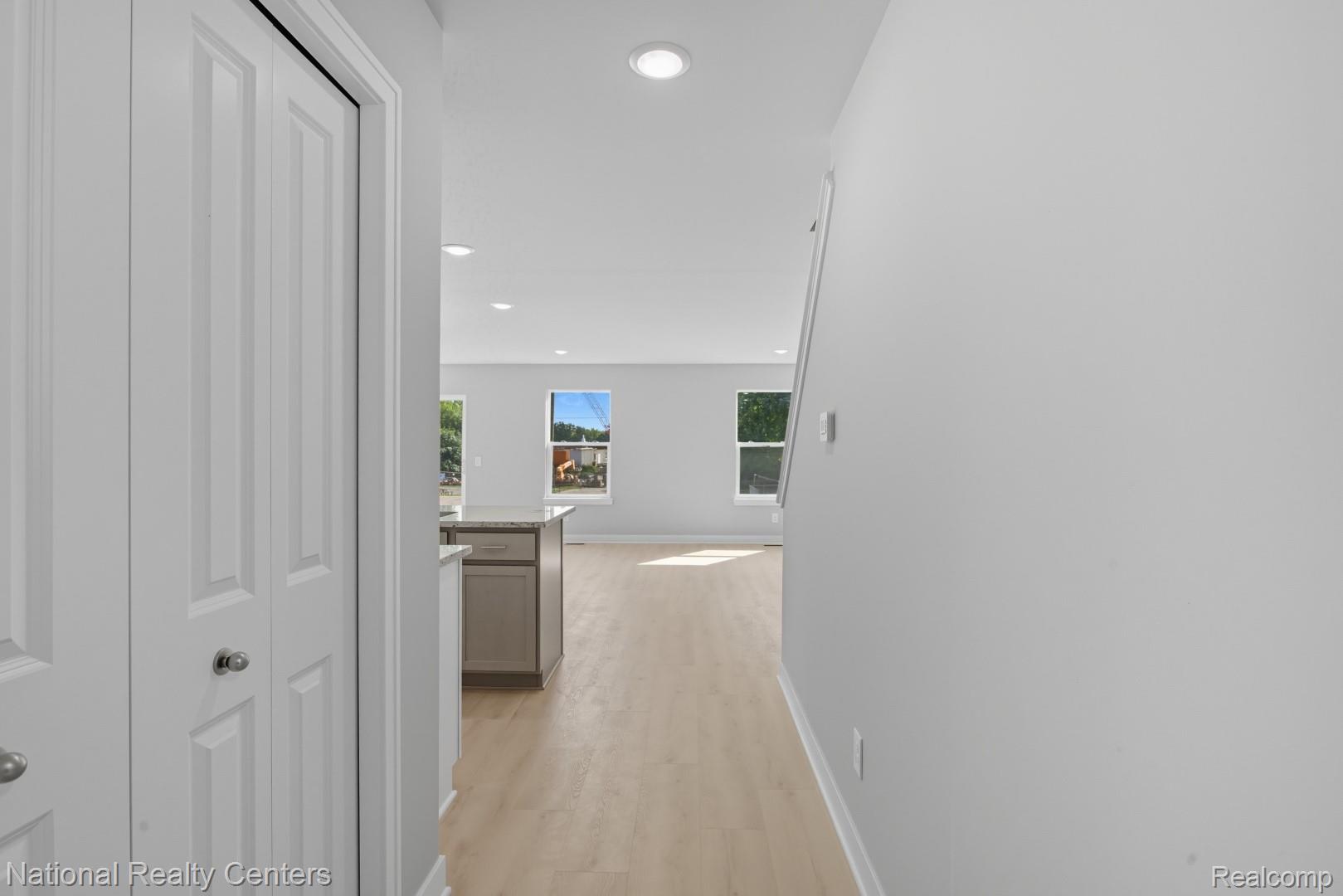 Recessed lighting, wood-finish flooring, white paneled doors, light grey wall paint, and a kitchen island with a stone countertop
