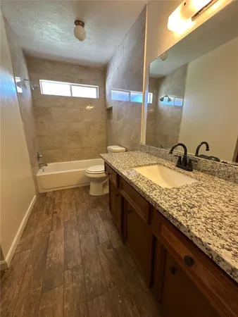 a bathroom with a granite countertop sink a toilet a mirror and bathtub