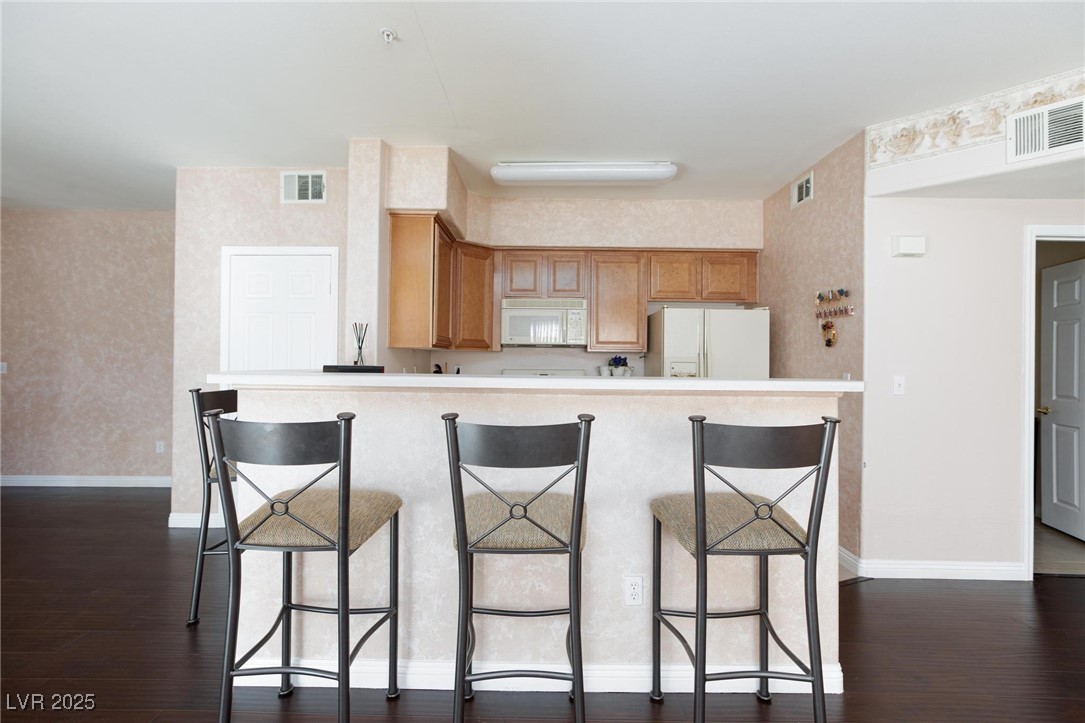 7185 South Durango Drive, Unit 201 Las Vegas, NV 89113 - Photo 9 of 27 Kitchen featuring white appliances, dark wood finished floors, light countertops, and a breakfast bar area