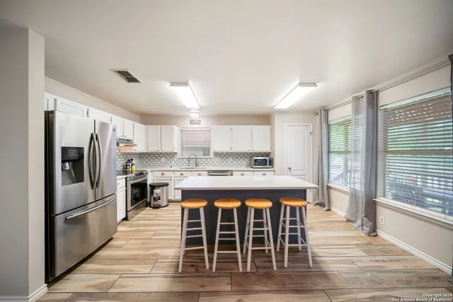 a large kitchen with kitchen island granite countertop a refrigerator a stove a sink dishwasher and white cabinets with wooden floor