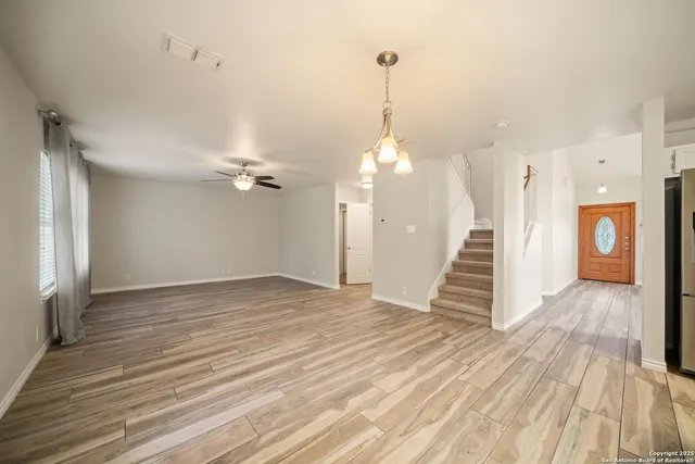 a view of an empty room with wooden floor and a ceiling fan